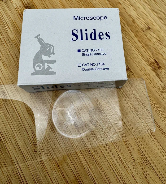 Boîte de lames concaves pour microscope avec une lame transparente au premier plan sur fond en bois.
