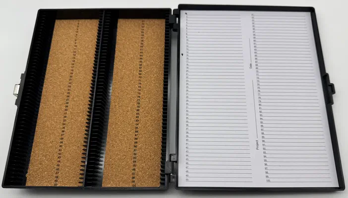 Boîte ouverte à lames de microscopie avec deux compartiments en liège et une liste d'archivage.