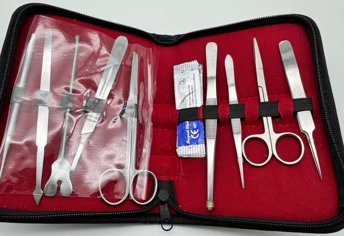 Trousse à outils de laboratoire ouverte contenant des ciseaux, spatules et pinces métalliques disposées dans un étui rouge.
