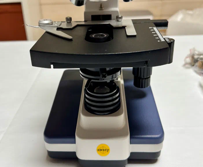 Vue de face d'un microscope montrant la platine, le diaphragme et le condenseur.