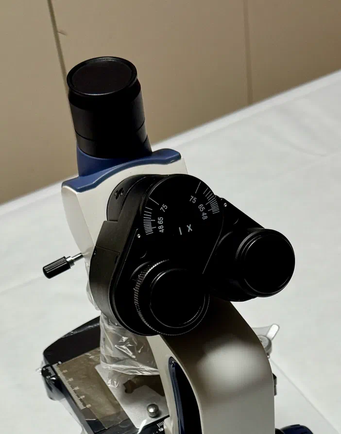 Détail de la tête d'un microscope avec un tube vertical pour caméra en arrière-plan