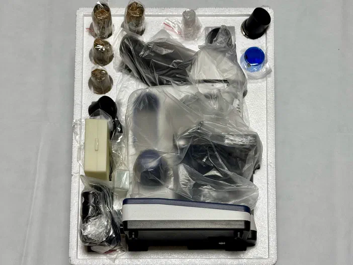 Un microscope et ses accessoires sont soigneusement emballés dans du polystyrène blanc.
