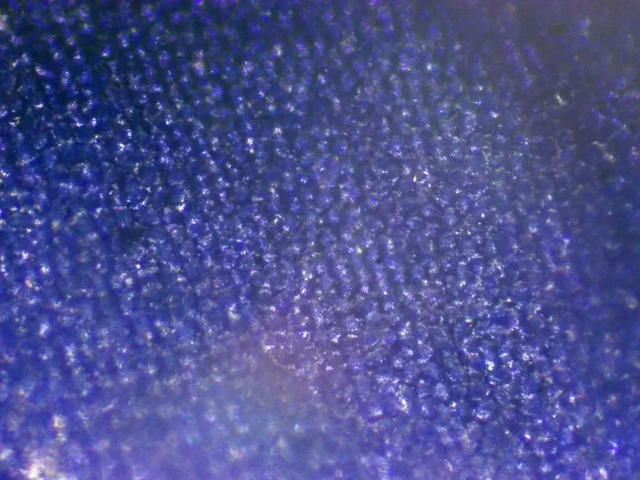Vue microscopique d'une surface bleue texturée avec un halo lumineux en bas causé par le masque de lumière